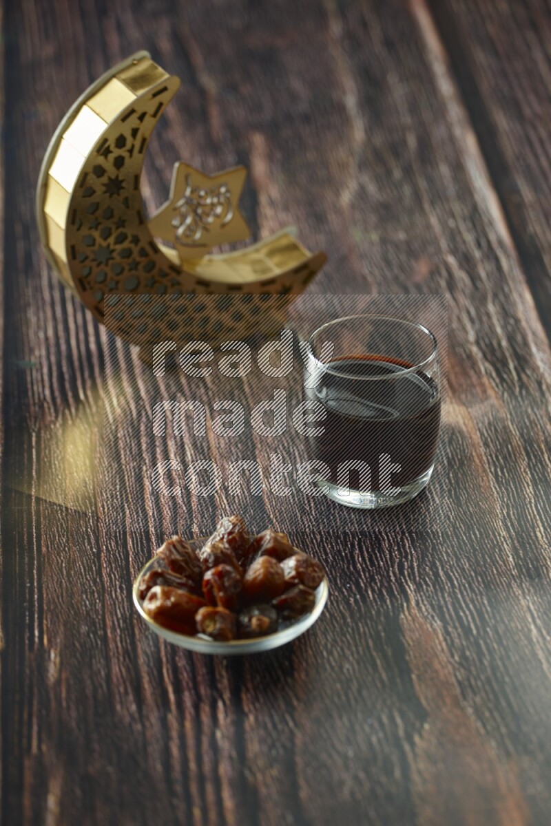 A wooden golden crescent lantern with different drinks, dates, nuts, prayer beads and quran on brown wooden background