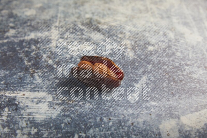 one almond stuffed madjoul dates on a rustic blue background