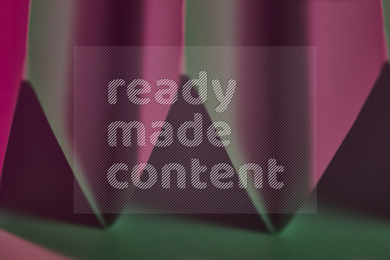 A close-up abstract image showing sharp geometric paper folds in green and pink gradients