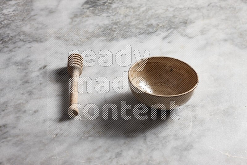 Multicolored pottery bowl with wooden honey dipper on the side on grey marble background