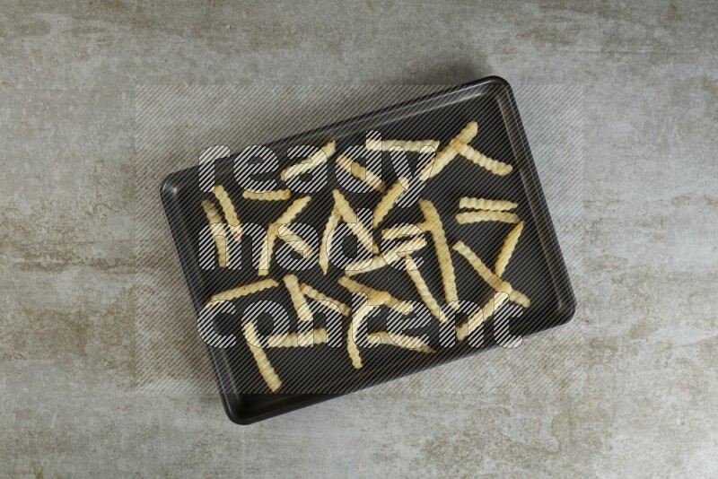 crinkle fries in a black stainless steel rectangle tray on grey textured counter top