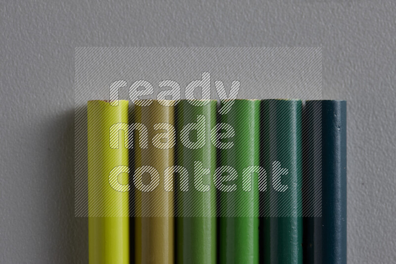 A collection of colored pencils arranged showcasing a gradient of green hues on grey background
