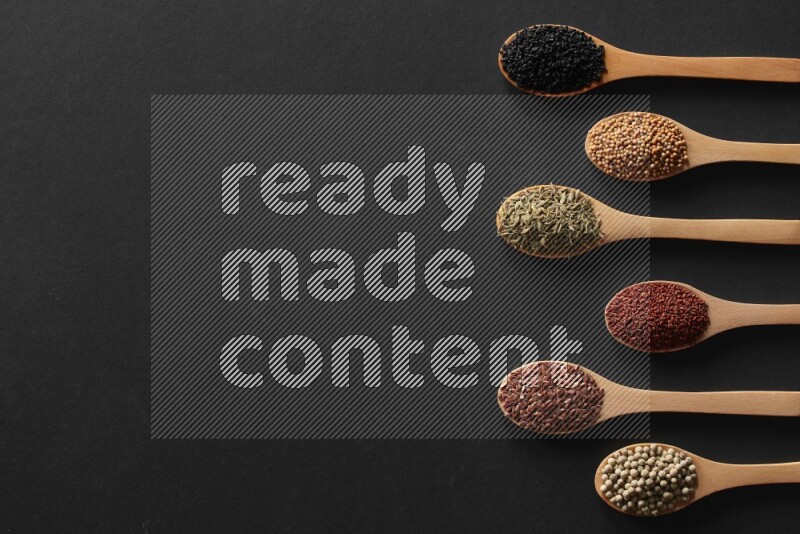 wooden spoons filled with white peppers, mustard seeds, black seeds, garden cress, cumin and flax on black flooring