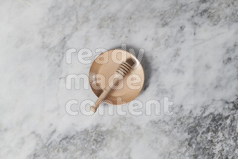 Beige pottery plate with wooden honey dipper in it on grey marble background