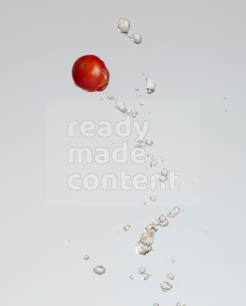 A single cherry tomato flying leaving a splash of water behind on a light blue background