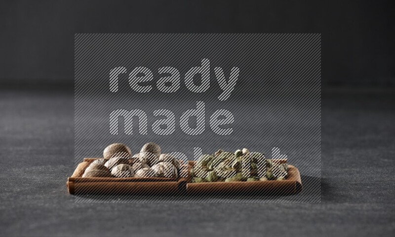 مربعان من أعواد القرفة ممتلئان بجوزة الطيب وحبوب الهيل علي خلفية سوداء