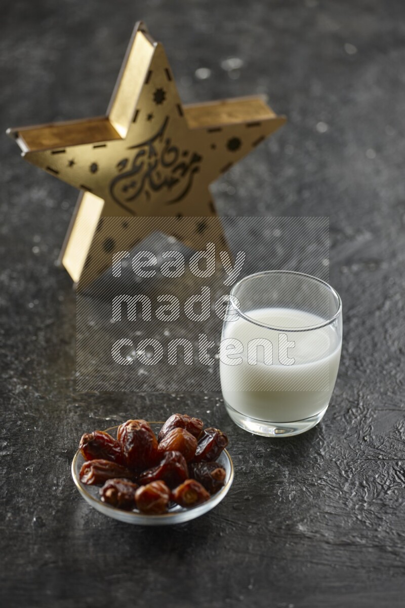 A wooden golden star lantern with different drinks, dates, nuts, prayer beads and quran on textured black background
