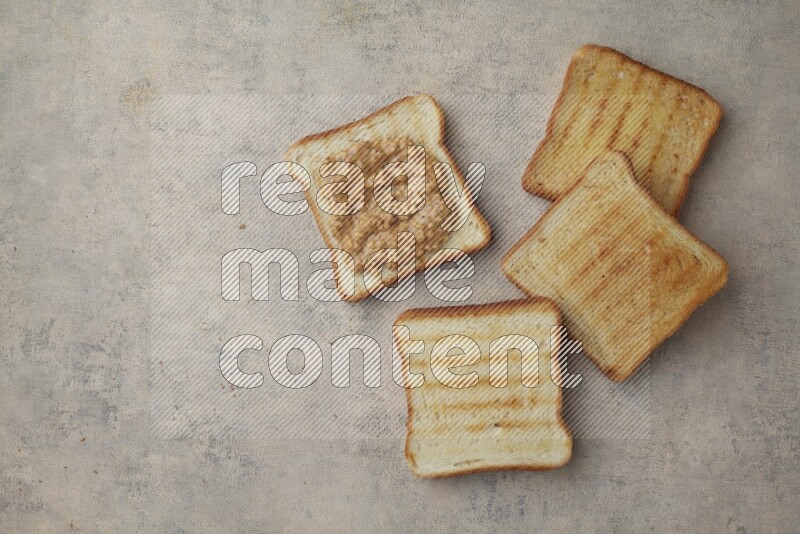 Crunchy peanut butter on a toasted white toast and toasted white toast slices on a light blue textured background