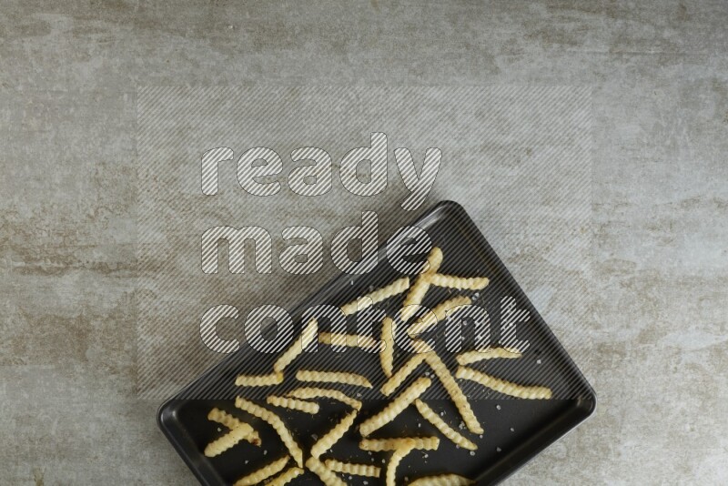 crinkle fries in a black stainless steel rectangle tray on grey textured counter top
