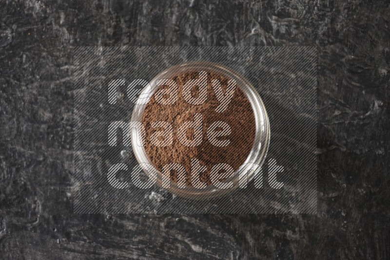 A glass jar full of cloves powder on a textured black flooring