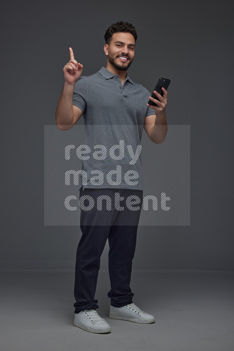 A man wearing casual standing and using his phone and making multi hand gestures eye level on a gray background