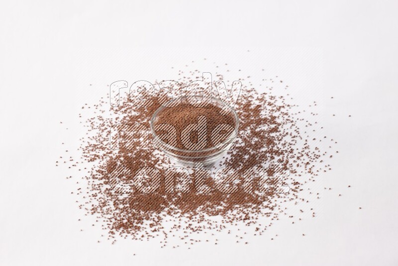 A glass bowl full of garden cress seeds with more seeds spread on a white flooring