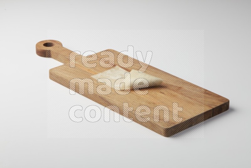 One uncooked samosa on a wooden cutter on a white background
