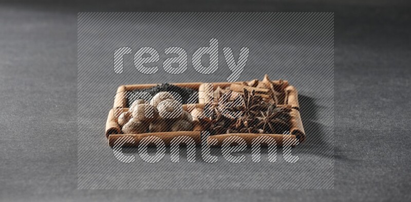 4 squares of cinnamon sticks full of black seeds, cinnamon, star anise and nutmegs on black flooring