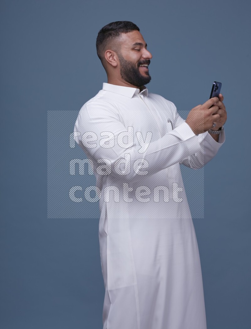 A man Texting on Blue Background wearing Saudi Thob