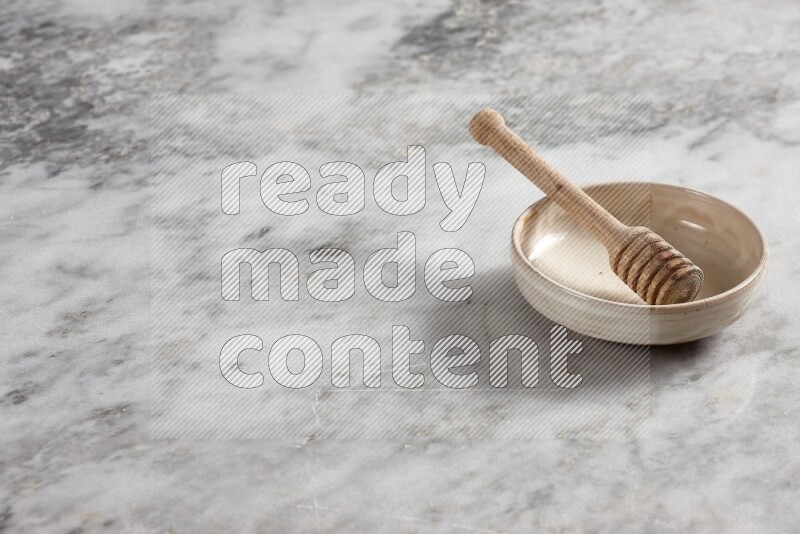 Beige pottery bowl with wooden honey dipper in it on grey marble background