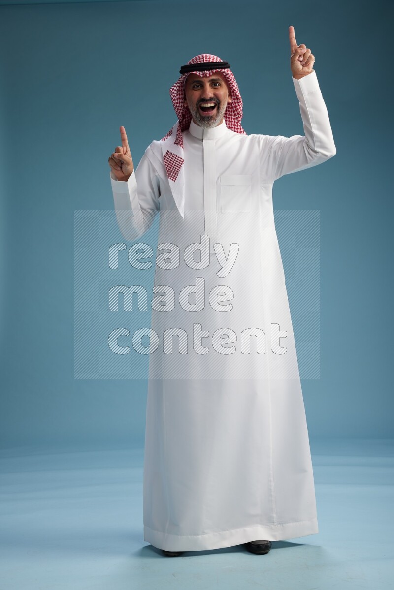 Saudi man wearing thob and shomagh posing to the camera on blue background