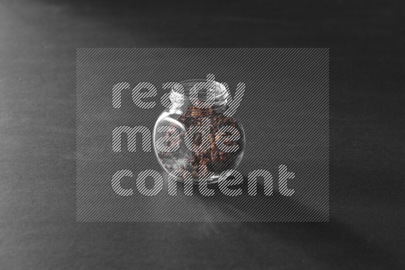 A glass spice jar full of cloves on black flooring