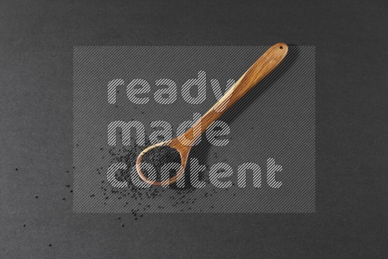 ملعقة خشبية كبيرة ممتلئة بحبة البركة مع بعض الحبوب منتشرة بجانبها على أرضية سوداء