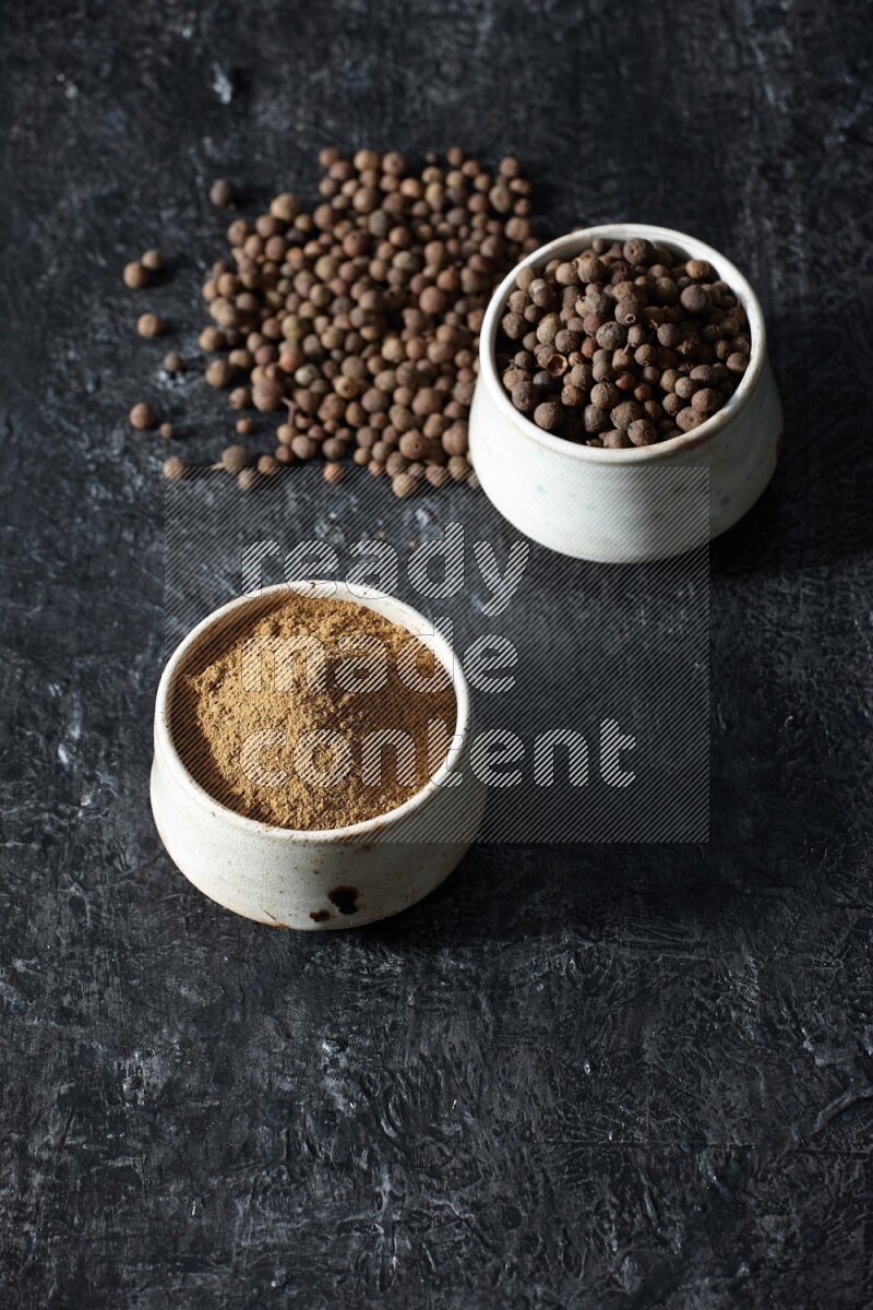 2 beige bowls, one full of allspice powder and the other full of whole balls and both spread on a textured black flooring