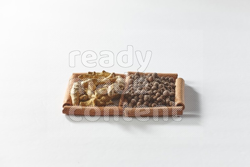 مربعان من أعواد القرفة ممتلئان ببهار الفلفل الحلو وأصابع الكركم علي خلفية بيضاء