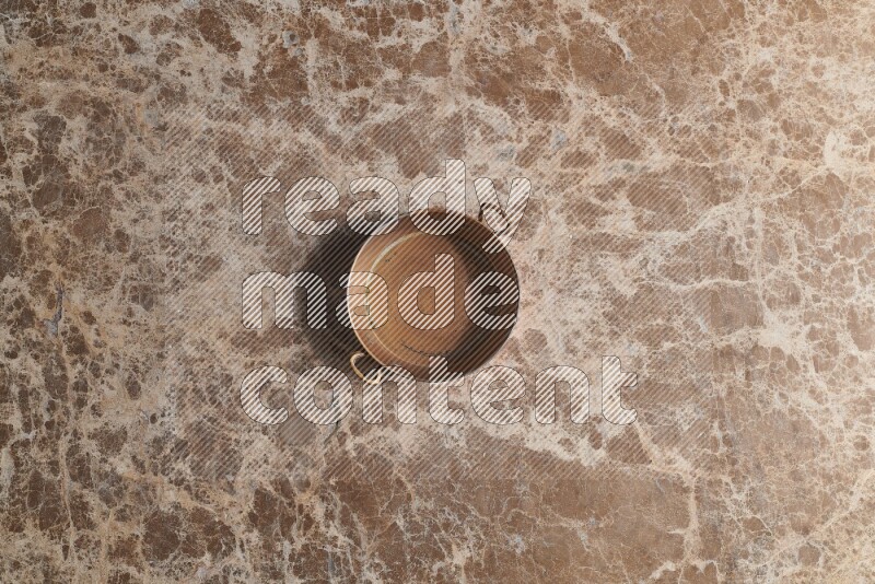 A small copper pan on beige marble background