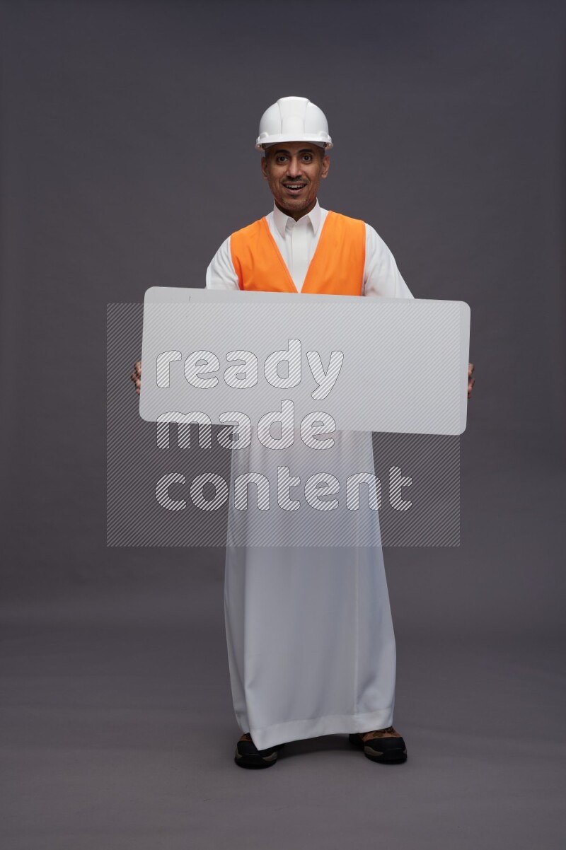 Saudi man wearing thob with engineer vest standing holding board on gray background