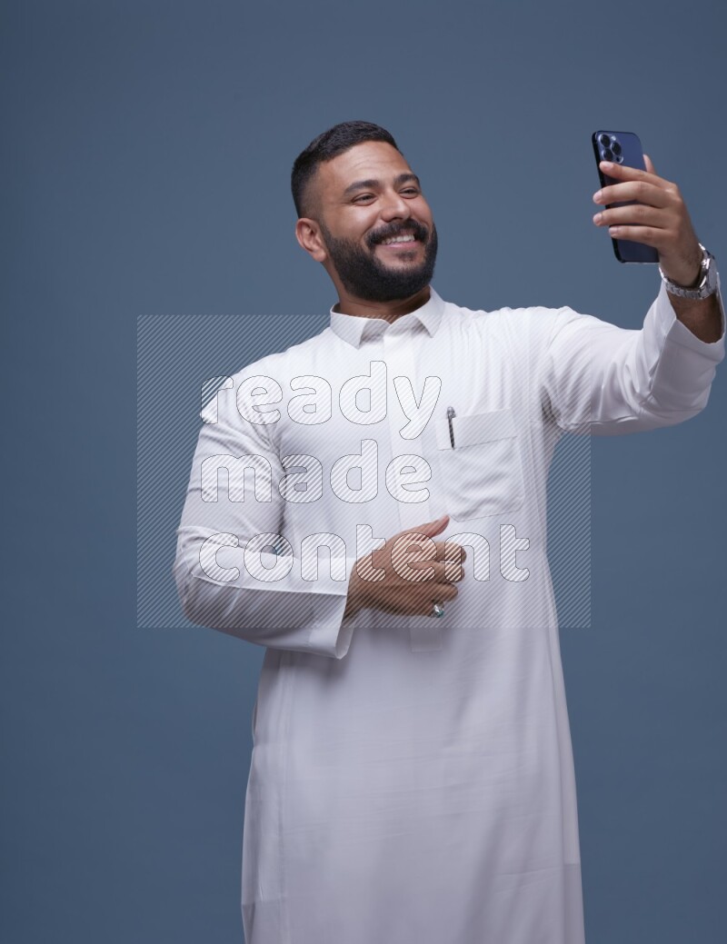 A Saudi man Taking A Selfie on Blue Background wearing Saudi Thob