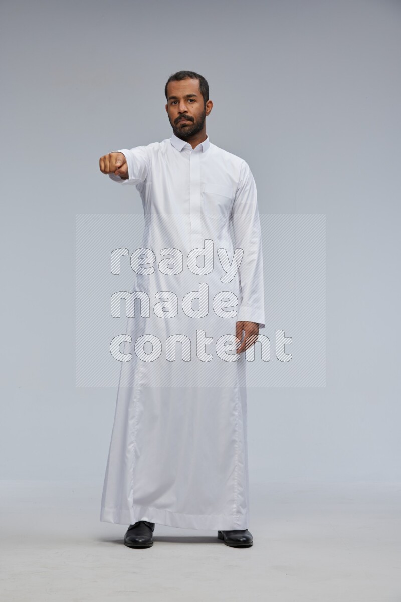 Saudi man Wearing Thob standing interacting with the camera on Gray background