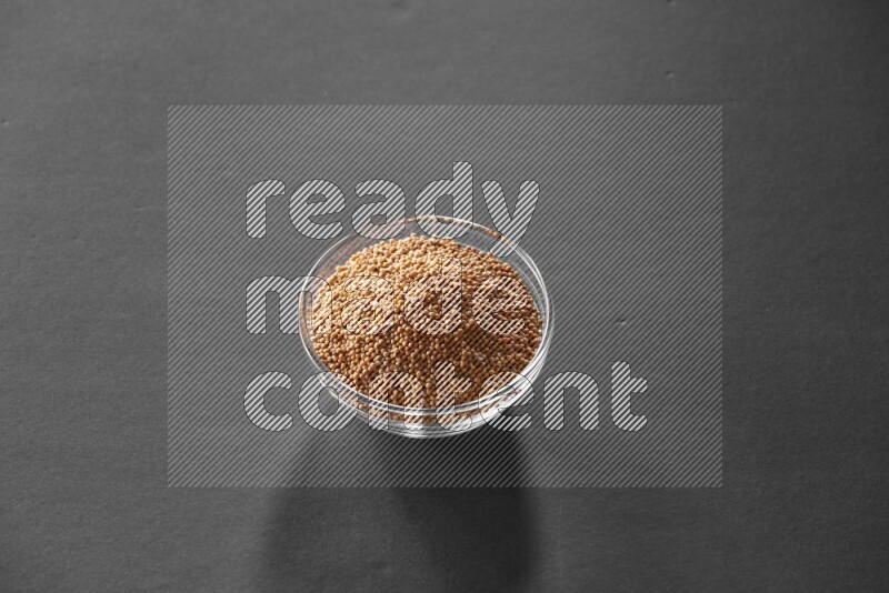 A glass bowl full of mustard seeds on black flooring