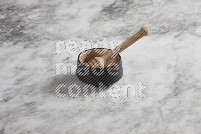 Black pottery bowl with wooden honey dipper in it on grey marble background