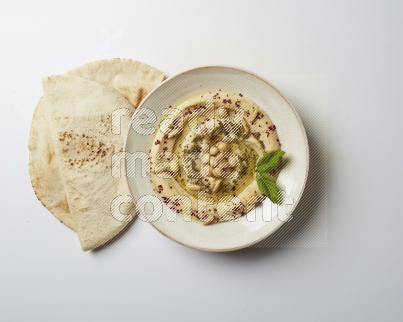 Hummus in a pottry plate garnished with zaatr & sumak on a white background