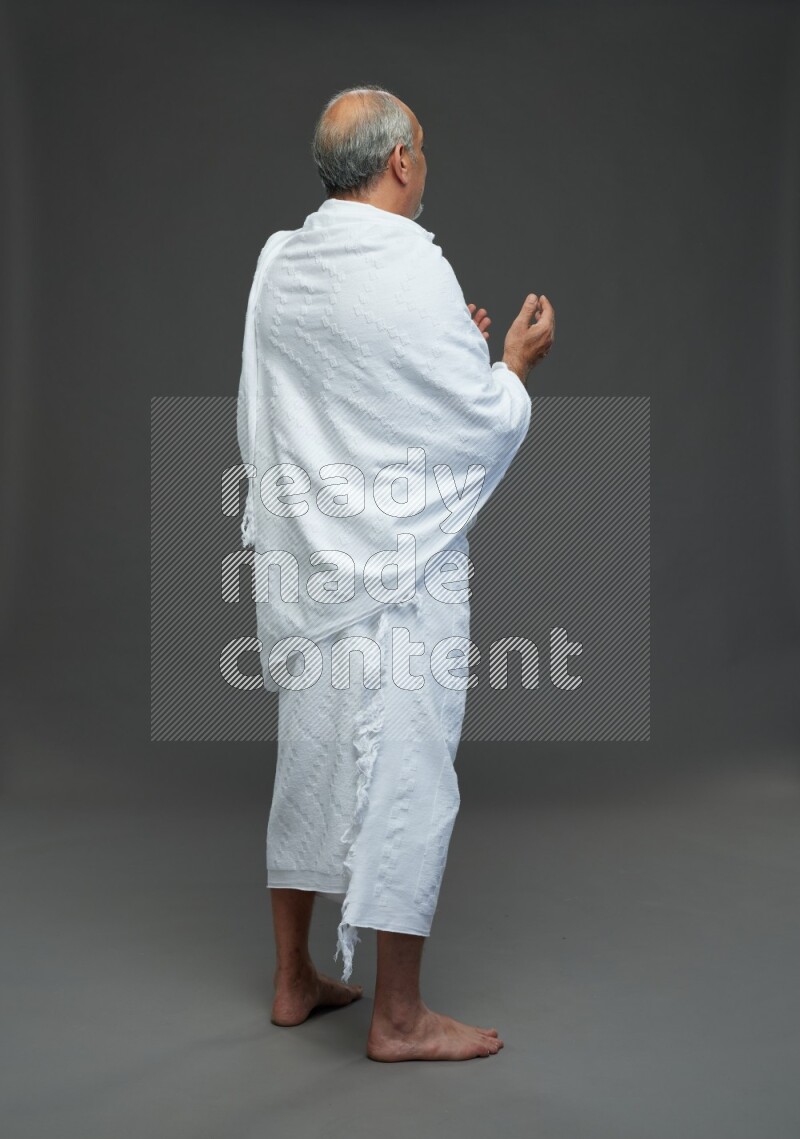 A man wearing Ehram Standing dua'a on gray background