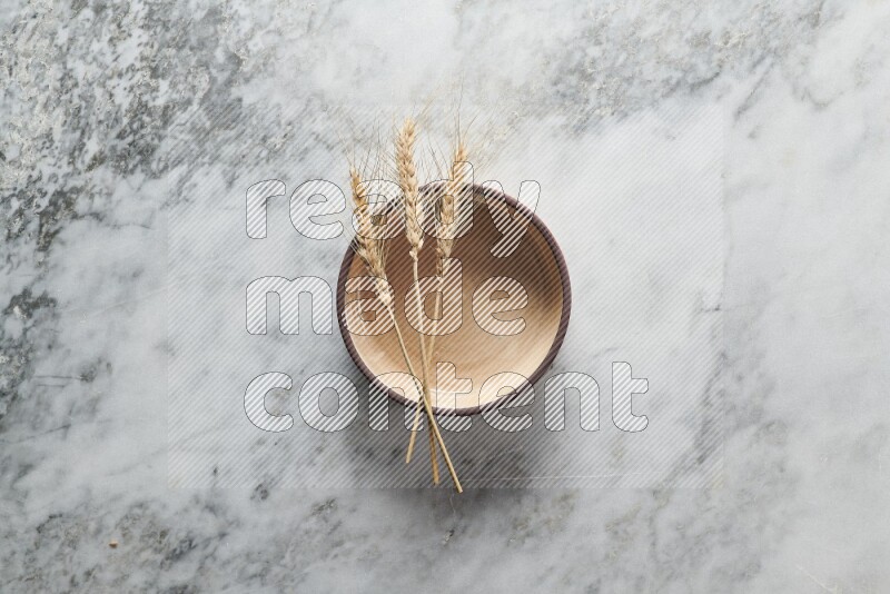 Wheat stalks on beige pottery oven bowl on grey marble background