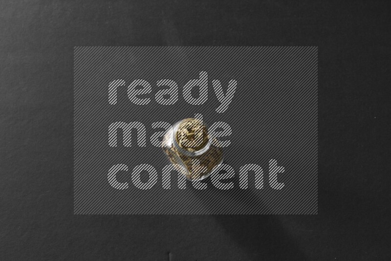 A glass spice jar full of cardamom on black flooring