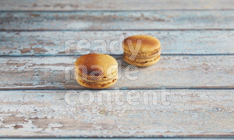 45º Shot of two Yellow Crème Brulée macarons on light blue wooden background