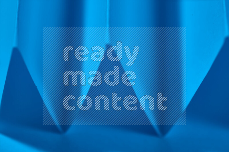 صورة مجردة مقربة تظهر طيات ورقية هندسية حادة بتدرجات اللون الأزرق