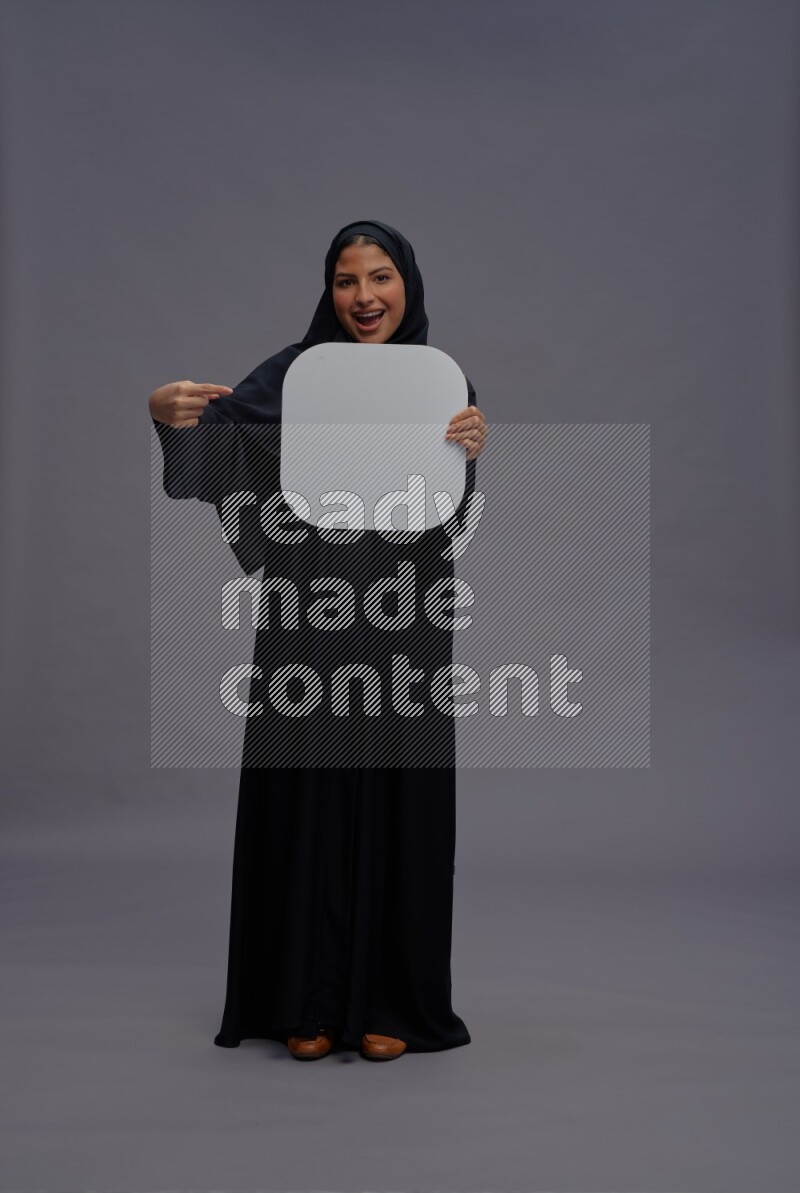Saudi woman wearing Abaya standing holding social media sign on gray background