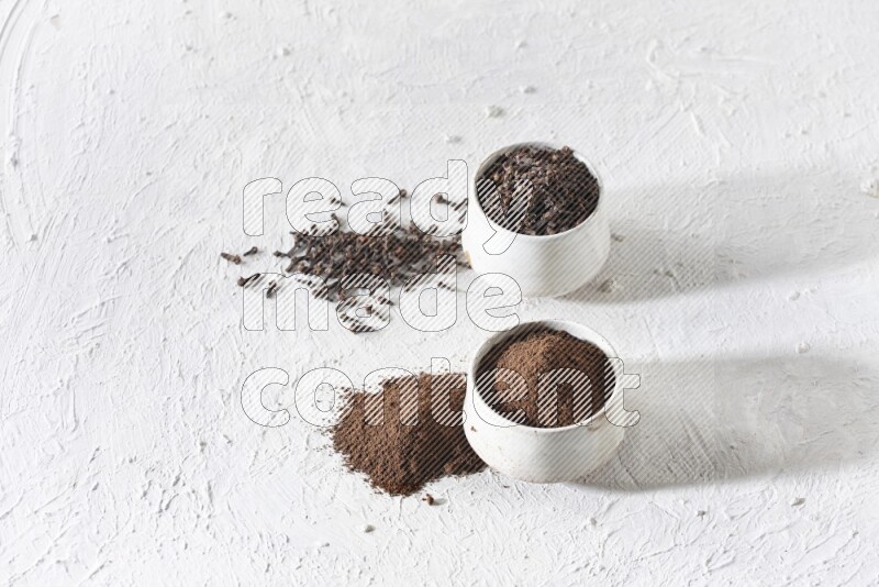 2 Beige ceramic bowls, one full of cloves and the other full of powder on textured white flooring