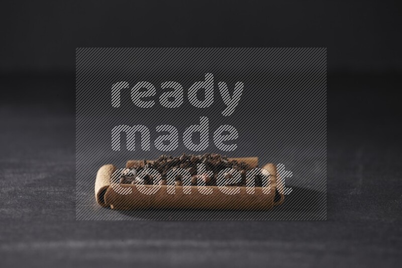A single square of cinnamon sticks full of cloves on black flooring