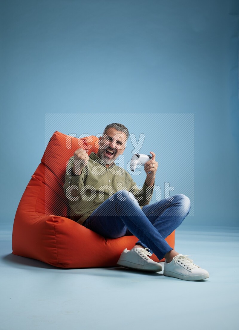 A man sitting on an orange beanbag and gaming with joystick
