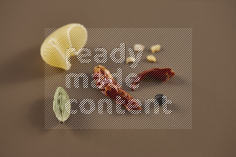Raw pasta with different ingredients such as cherry tomatoes, garlic, onions, red chilis, black pepper, white pepper, bay laurel leaves, rosemary and cardamom on beige background