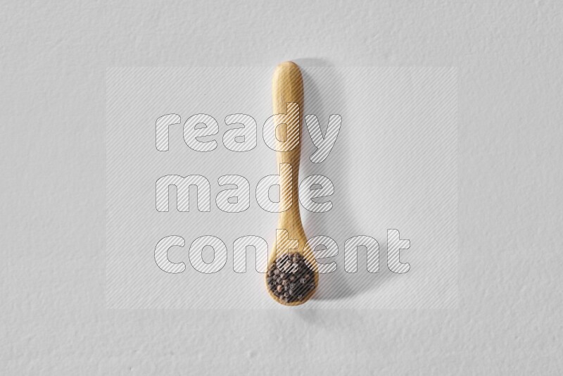 A wooden spoon full of black pepper on white flooring