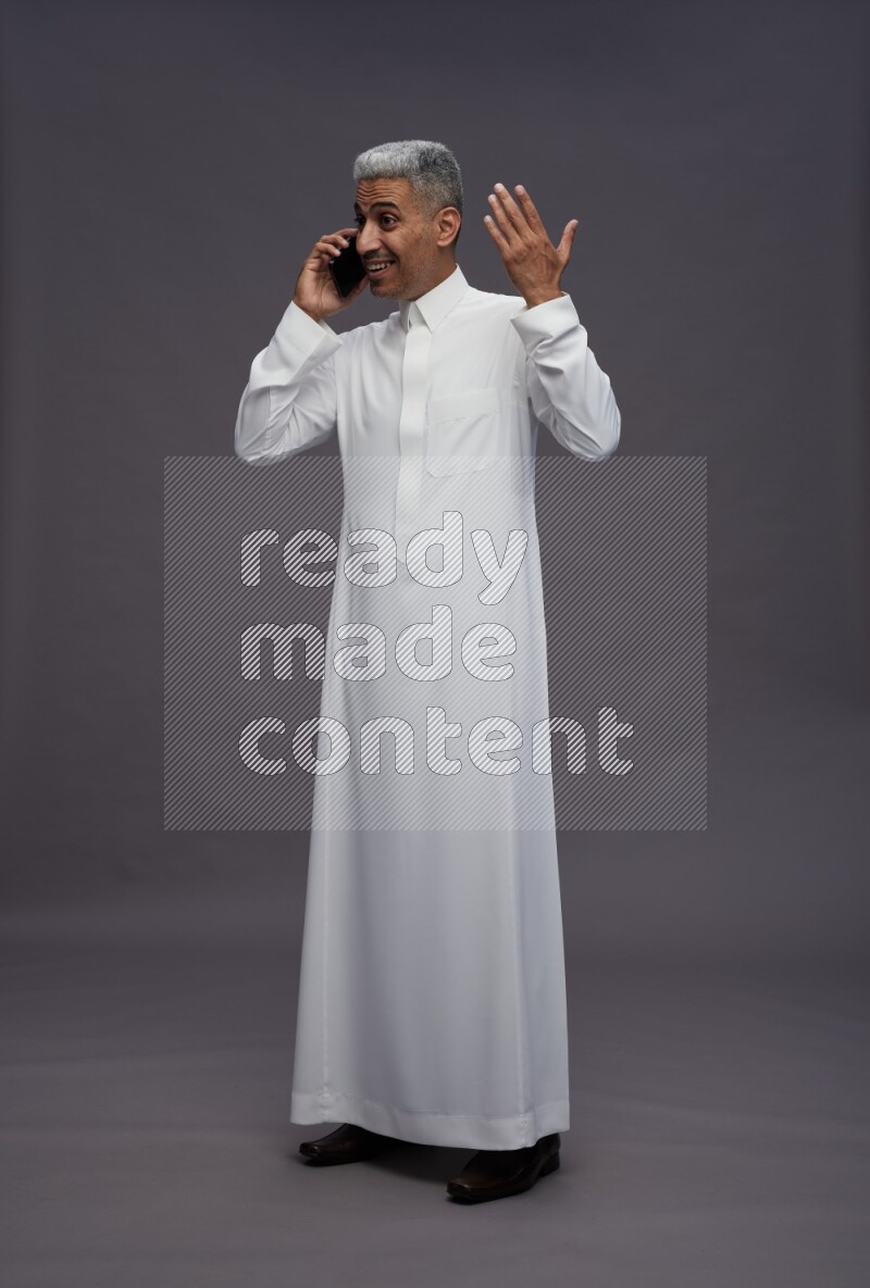 Saudi man wearing thob standing talking on phone on gray background