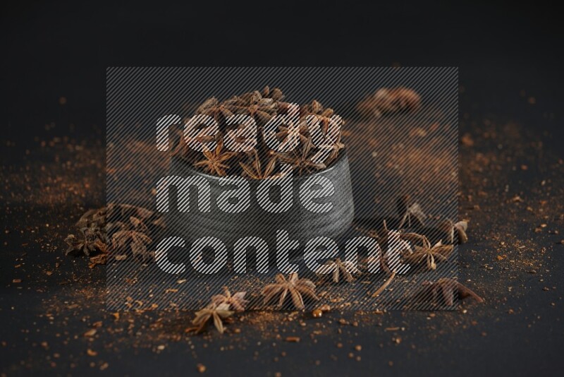 Star Anise in a black bowl with sprinkled anise on black flooring
