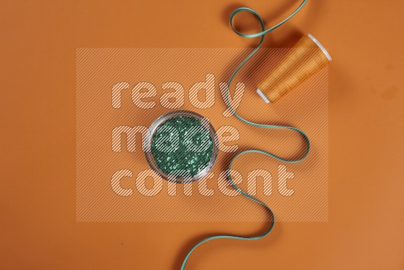 A green and orange collection of sewing and tailoring tools arranged on a orange background