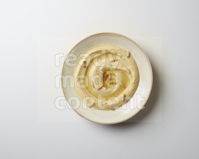 Hummus in a pottry plate garnished with pine nuts on a white background