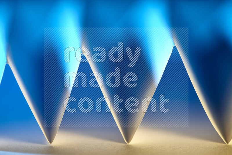 A close-up abstract image showing sharp geometric paper folds in blue gradients and warm tones