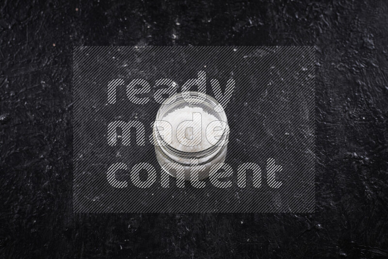 A glass jar full of coarse sea salt crystals on black background