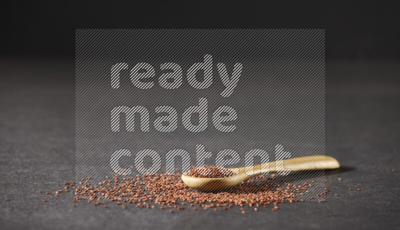 ملعقة خشبية ممتلئة ببذور حب الرشاد وبعض البذور متناثرة علي خلفية سوداء